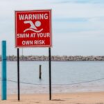 A warning sign on a beach next to a body of water