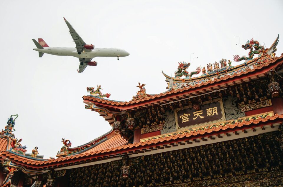 An airplane flies over a traditional Chinese temple in Xiamen, Fujian, blending modern and ancient architecture.
