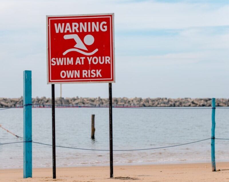 A warning sign on a beach next to a body of water