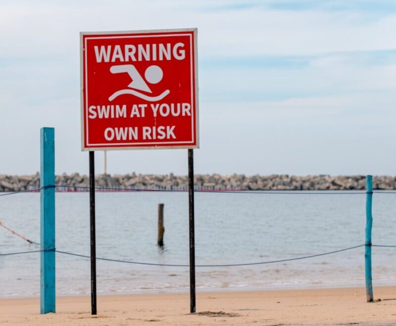 A warning sign on a beach next to a body of water